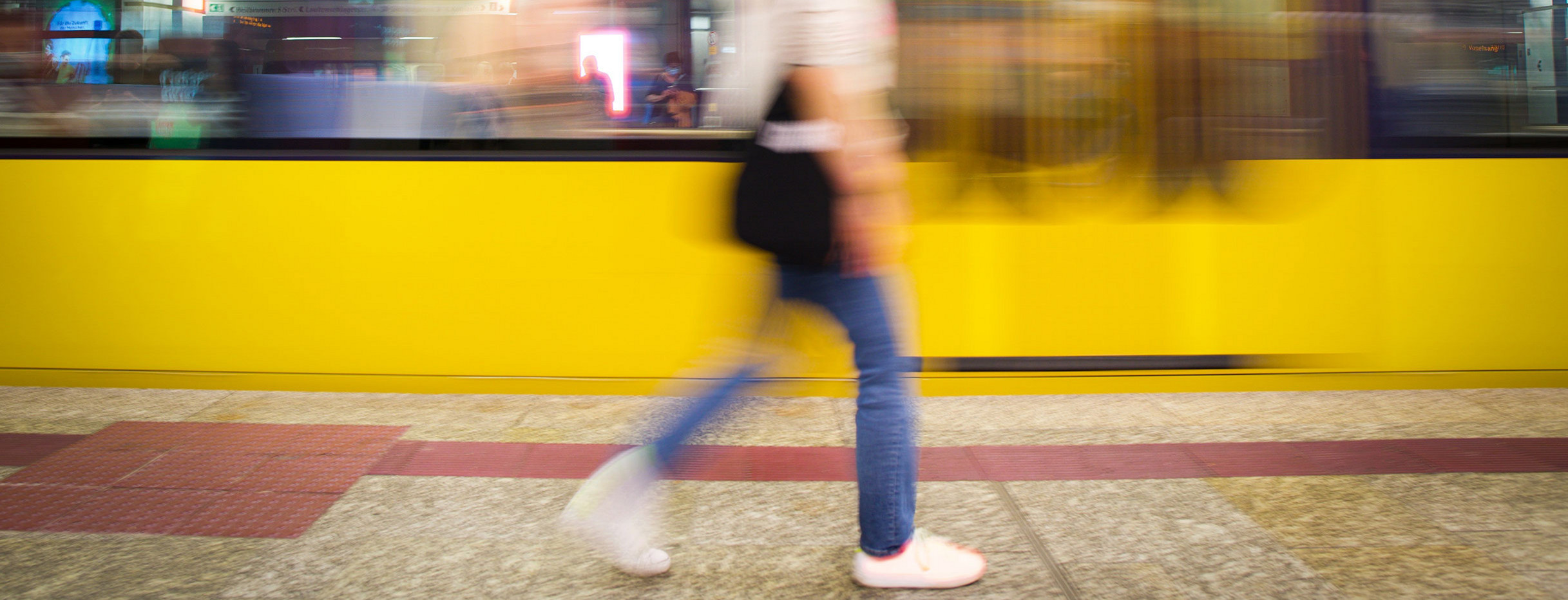 Verschwommenes Bild mit einer Frau, die an einem Bahnsteig entlangläuft während eine gelbe Bahn vorbeifährt.