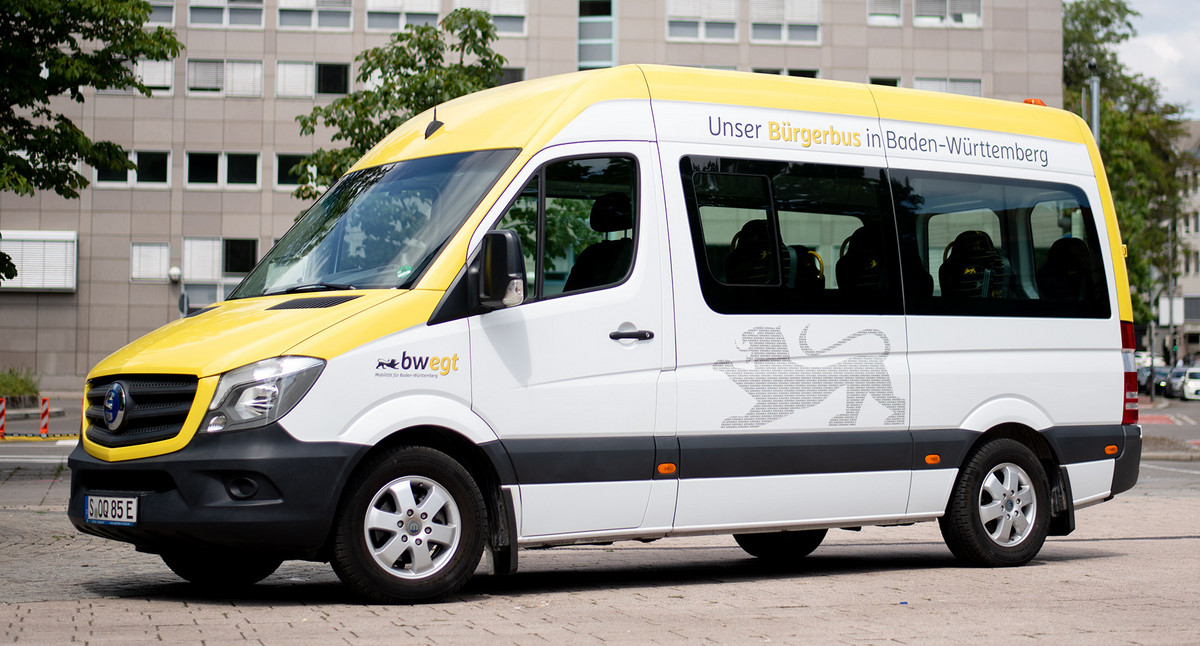 Ein kleiner weiß, gelber Transporter steht als Bürgerbus umgebaut auf einem Platz.