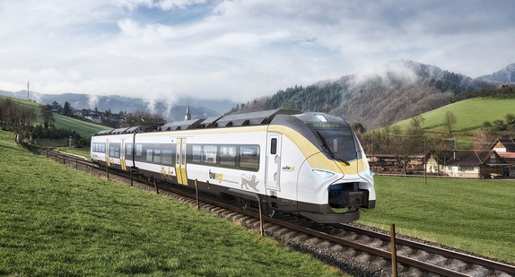 Ein weiß gelber Zug, Modell Mireo von Siemens, fährt auf Schienen durch eine grüne Landschaft.